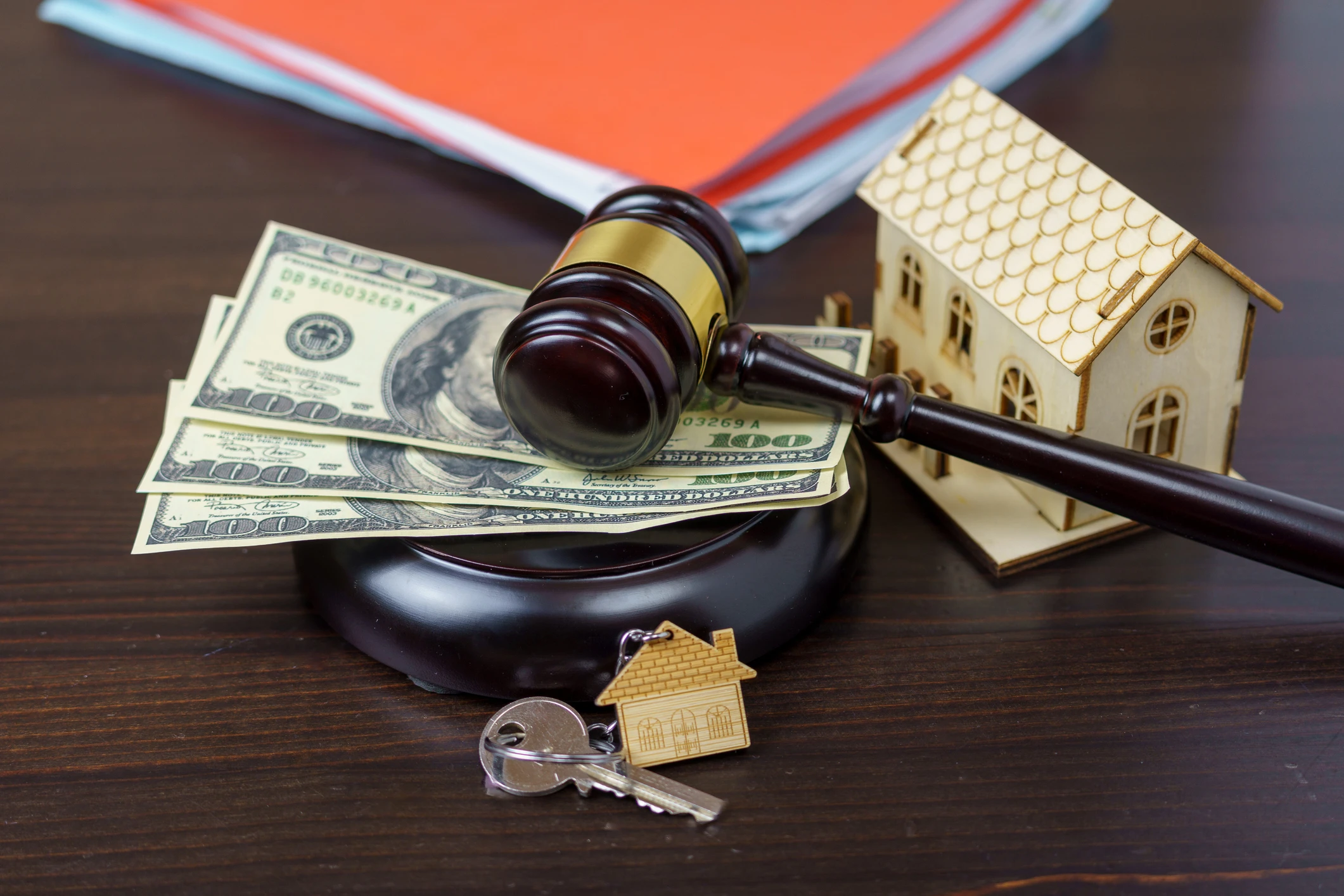 Gavel, money, house model, keys on table.