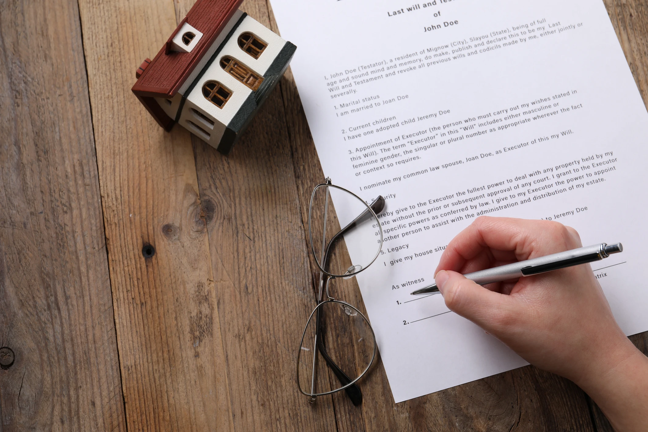 Hand signing document near miniature house.