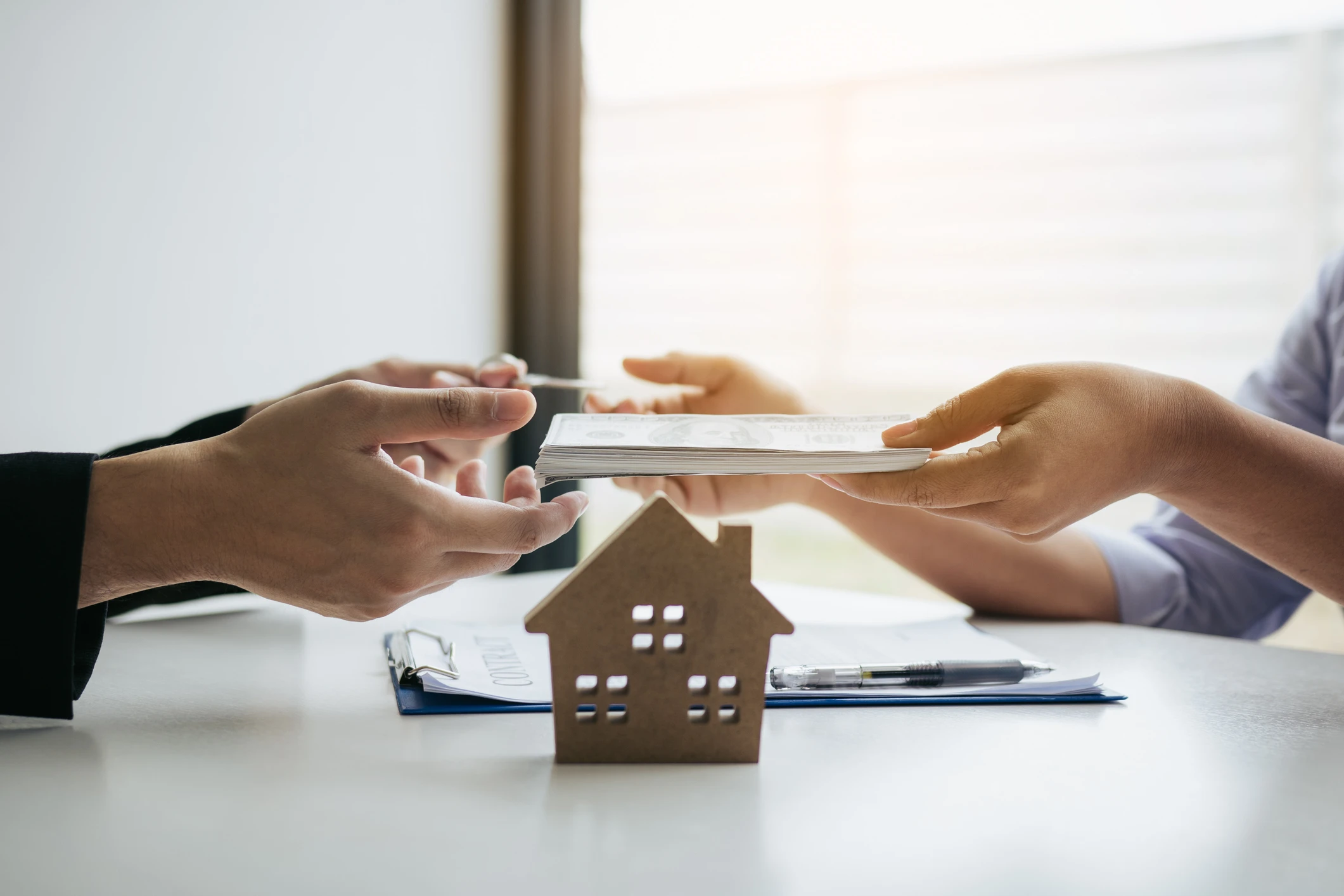 Hands exchanging documents over house model.