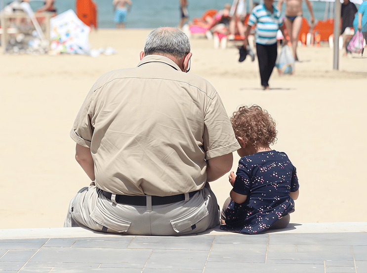 Older man and child sitting on beach.