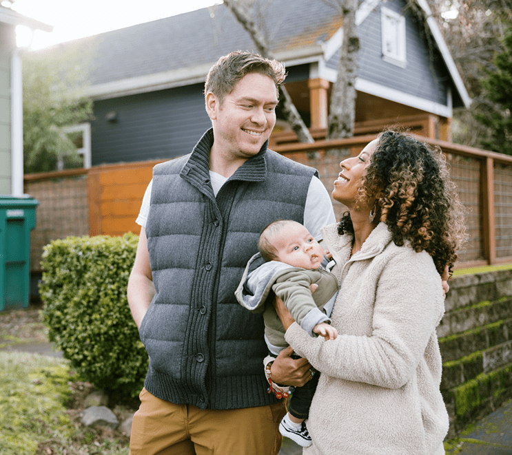 Smiling couple with baby in residential neighborhood.