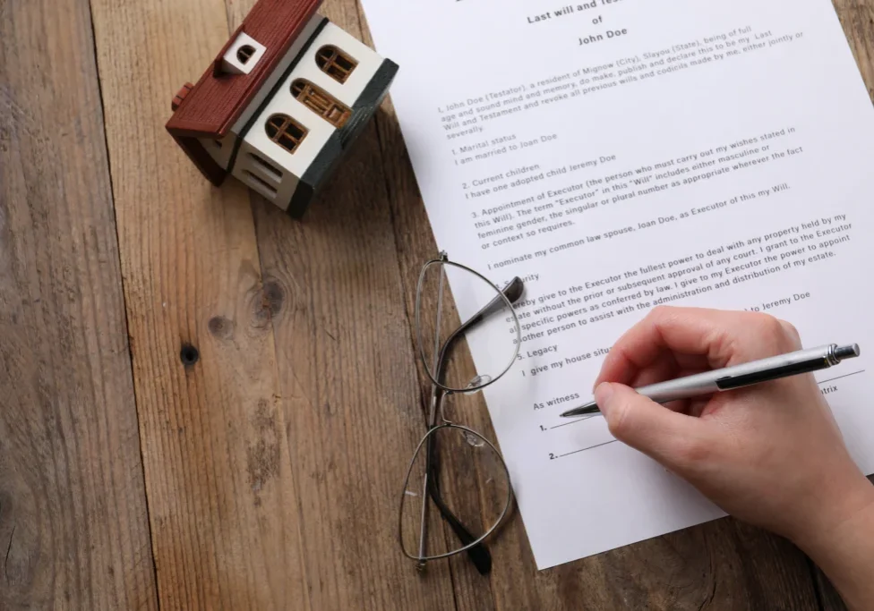 Hand signing document near miniature house.