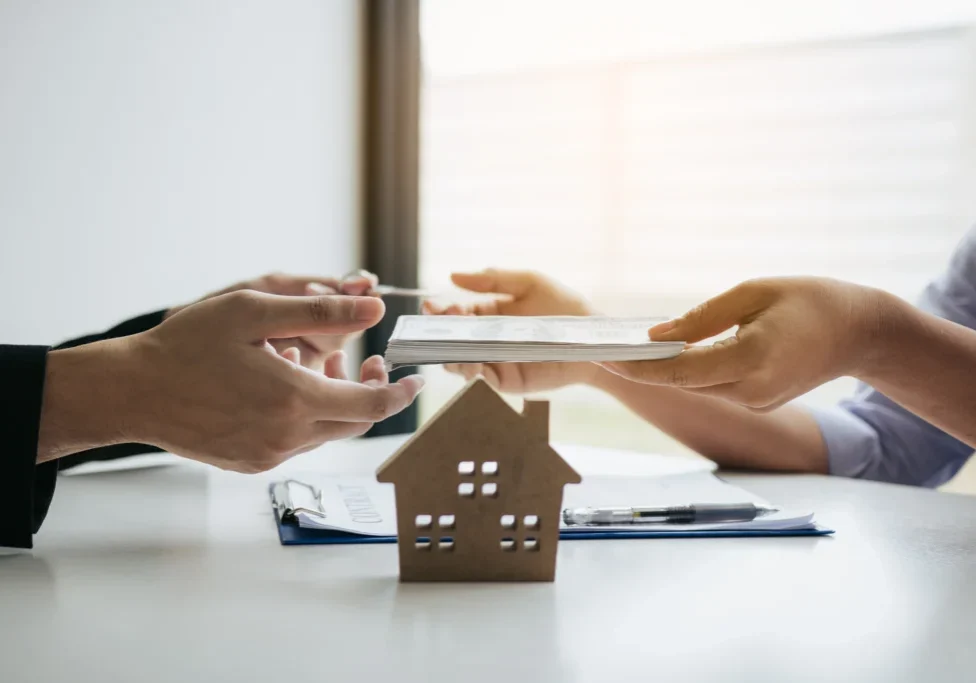 Hands exchanging documents over house model.